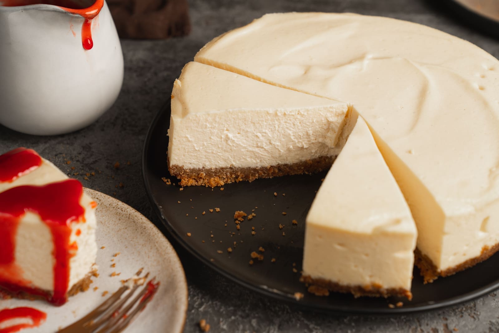 New York Cheesecake angeschnitten, daneben ein Stück mit Erdbeersauce