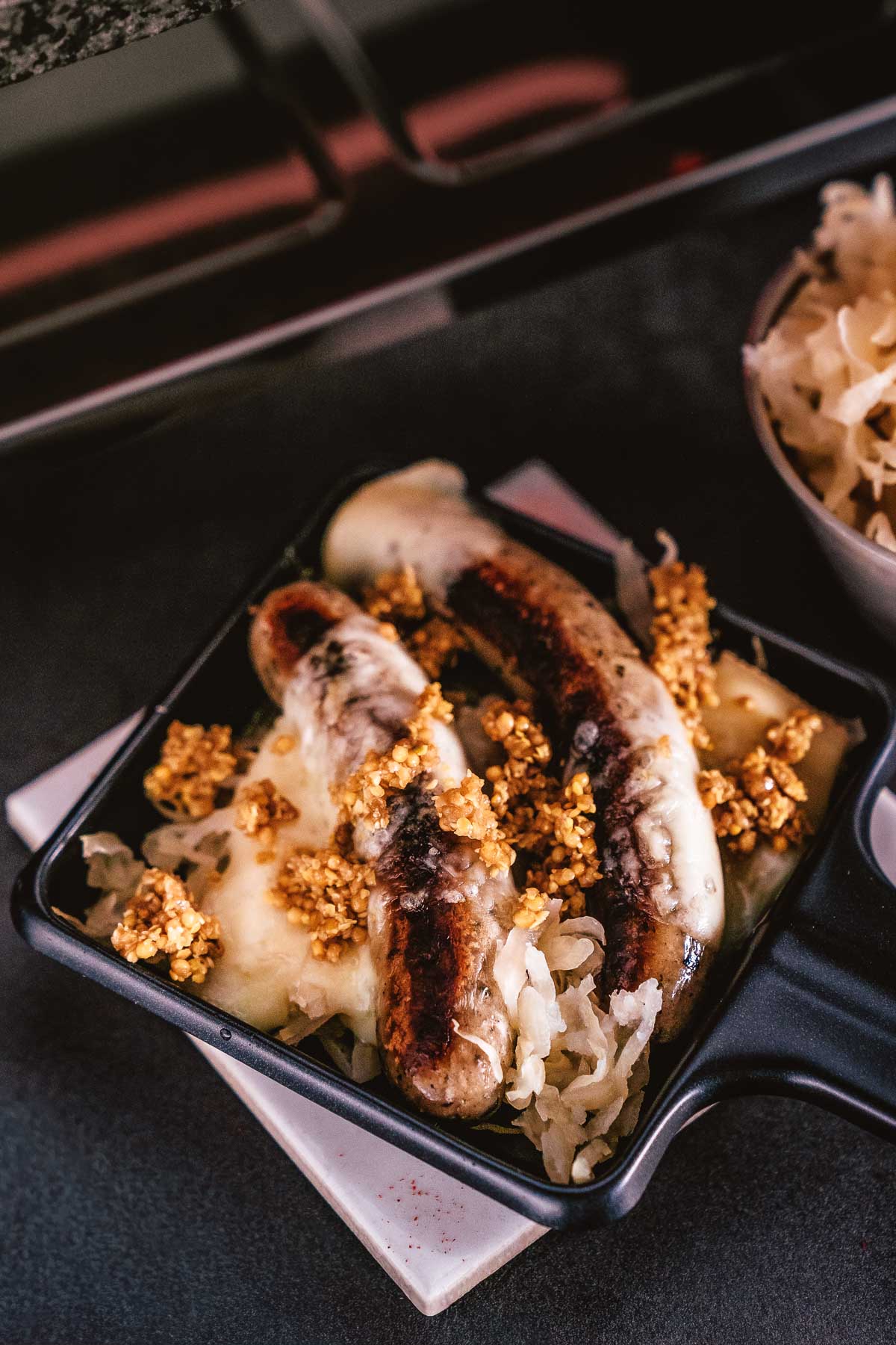 Raclette Pfännchen Ideen mit Bratwurst, Sauerkraut, geschmolzenem Käse und Crunch Topping