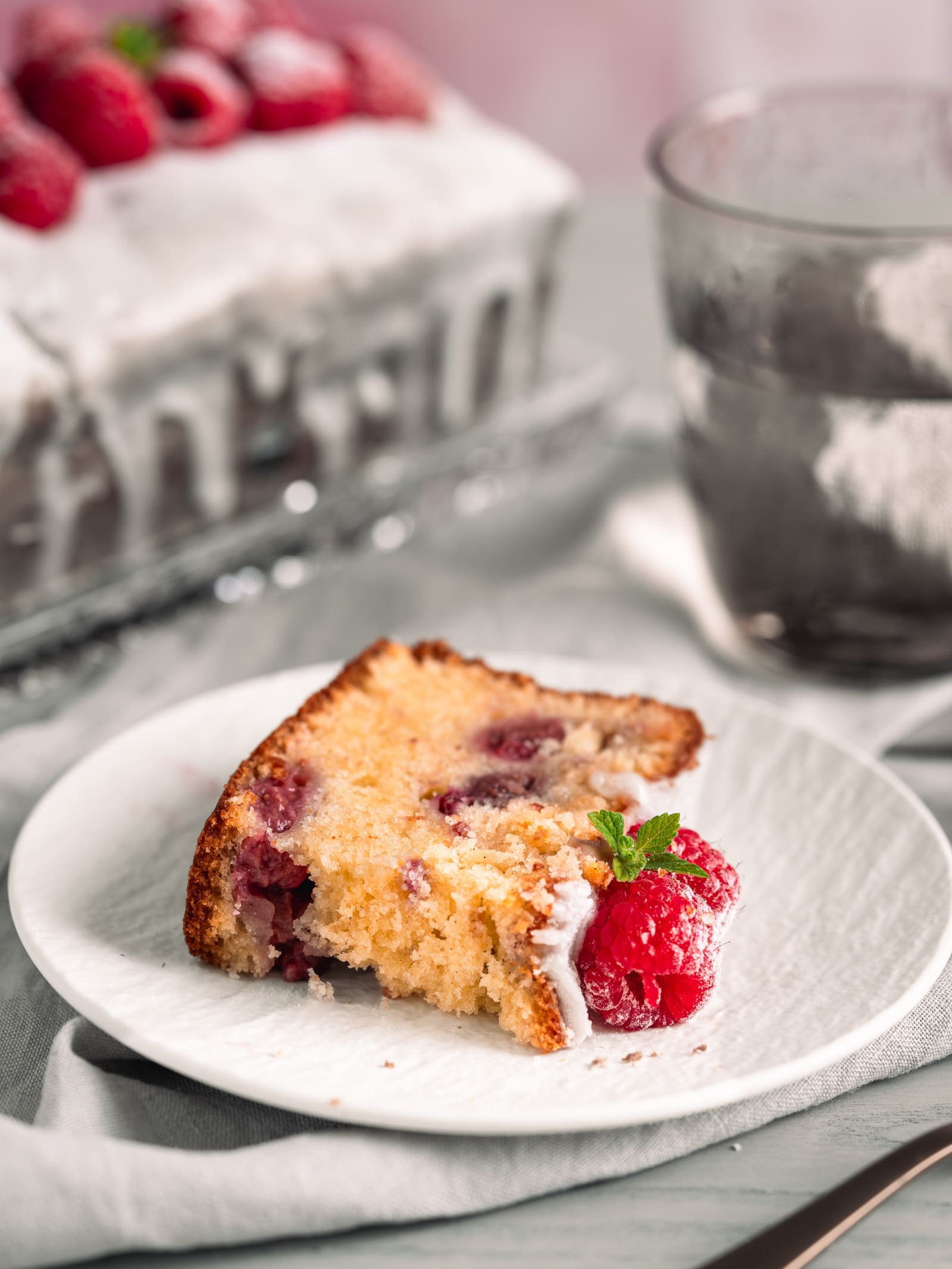 Angebissenes Stück Joghurt-Himbeerkuchen mit Himbeeren auf einem Teller